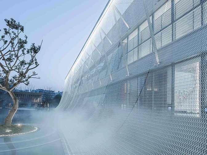 Metal mesh screen in front of a glazed building beside a landscaped water feature