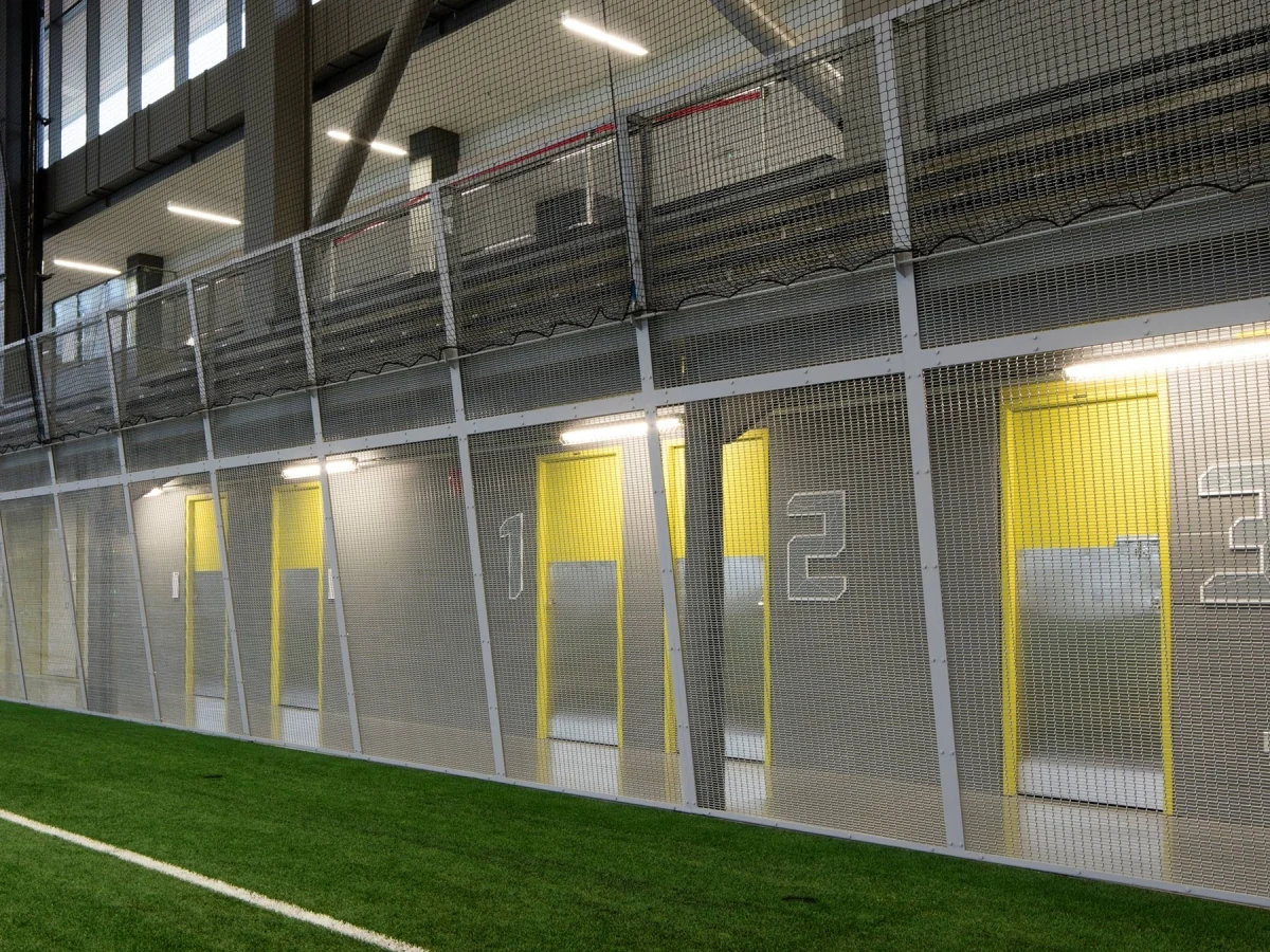 Framed metal mesh screens below an indoor mezzanine beside a sports area