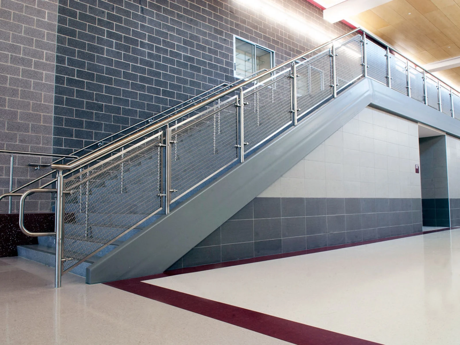Framed metal mesh infill along an interior stair and upper landing beside a brick wall