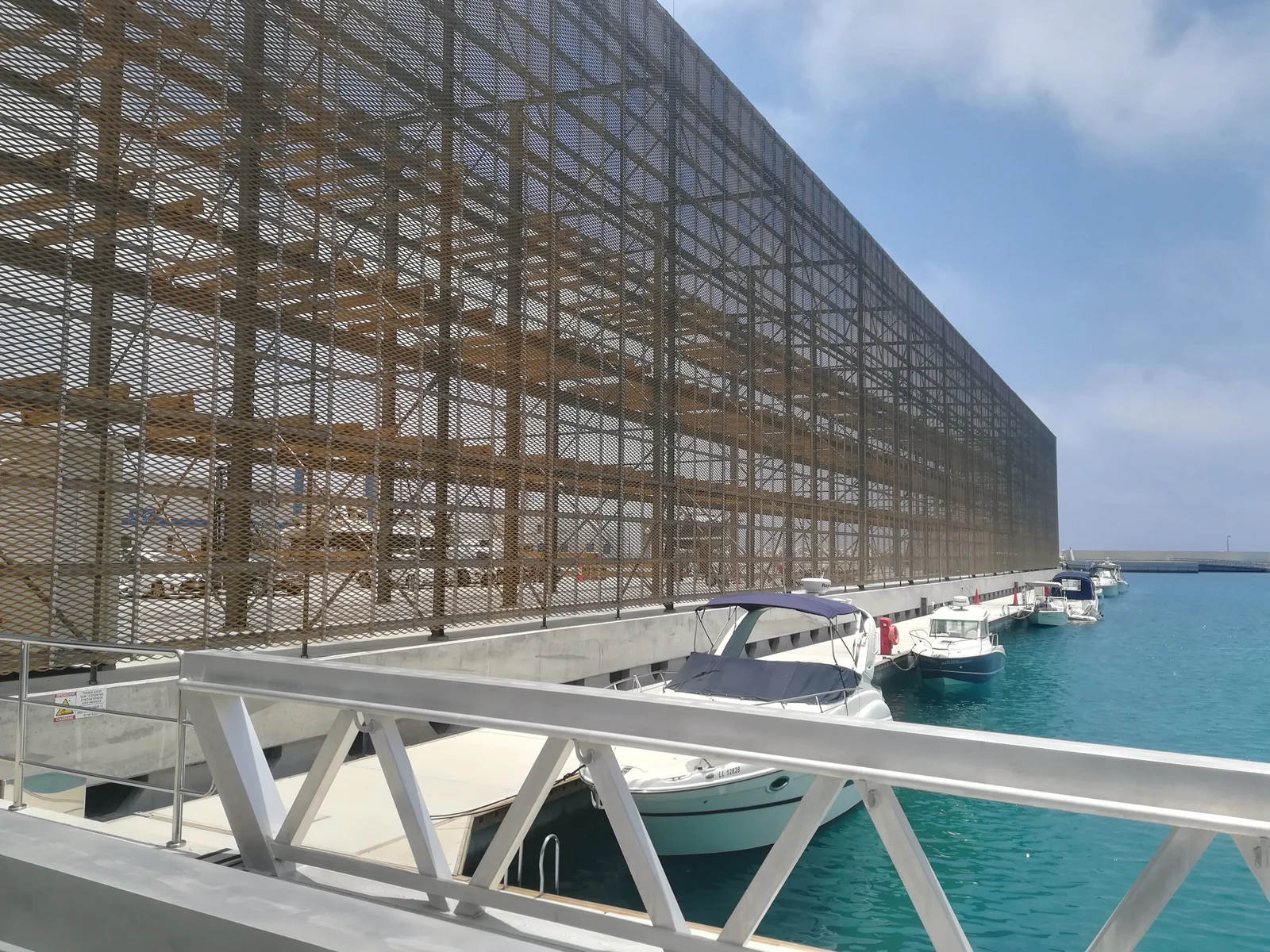 Expanded metal mesh screen over a glazed facade beside a waterfront