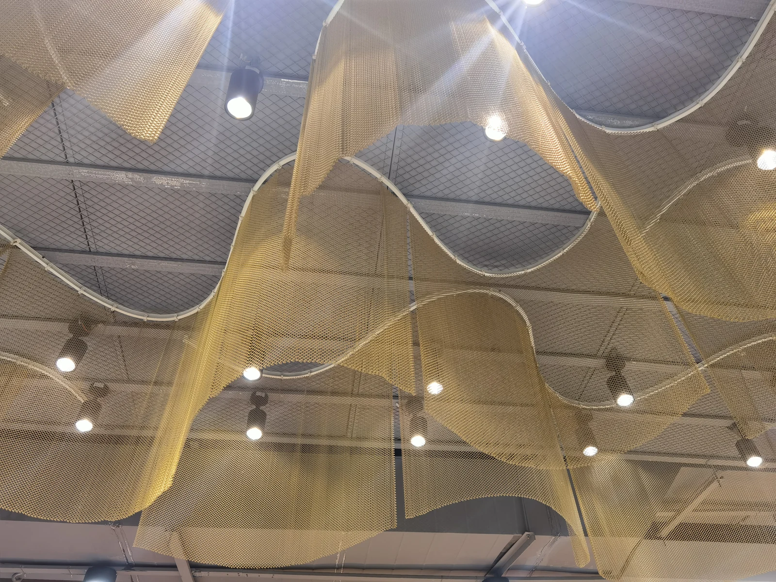 Metal coil mesh suspended in curved ceiling features beneath overhead lights
